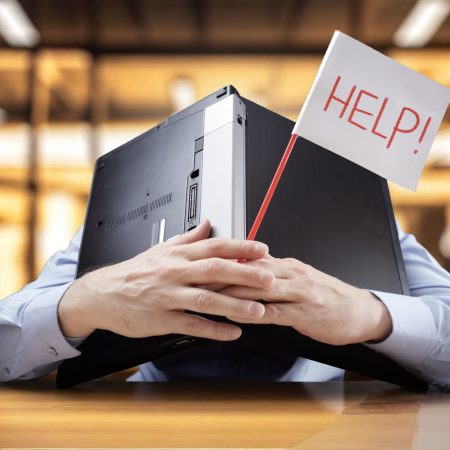 Frustrated and overworked businessman burying his head uner a laptop computer asking for help